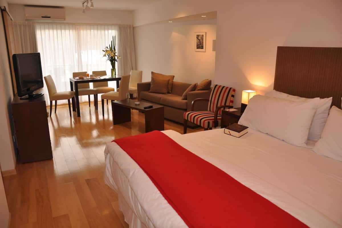 A hotel room with a large bed, a TV, a dining table with chairs, and a sofa.