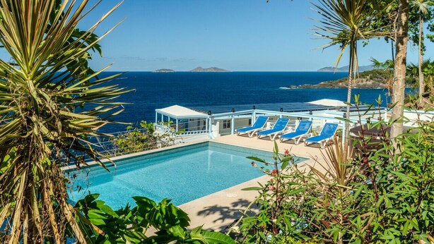 Una piscina con sillas azules y vista al océano.