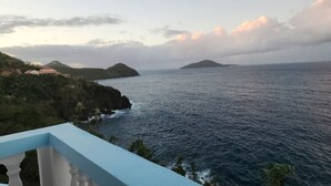 Une vue sur la côte, avec un balcon donnant sur la mer, une île lointaine et un bâtiment doté d’un toit rouge.