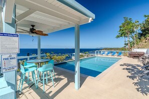 A pool area with clear blue water, a covered seating area with chairs, and a view of the ocean. - Dolphin Oceanfront Villa with Pool & Hot Tub! USVI (St Thomas)