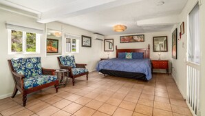A bedroom with a bed, two chairs, a nightstand, and a window.