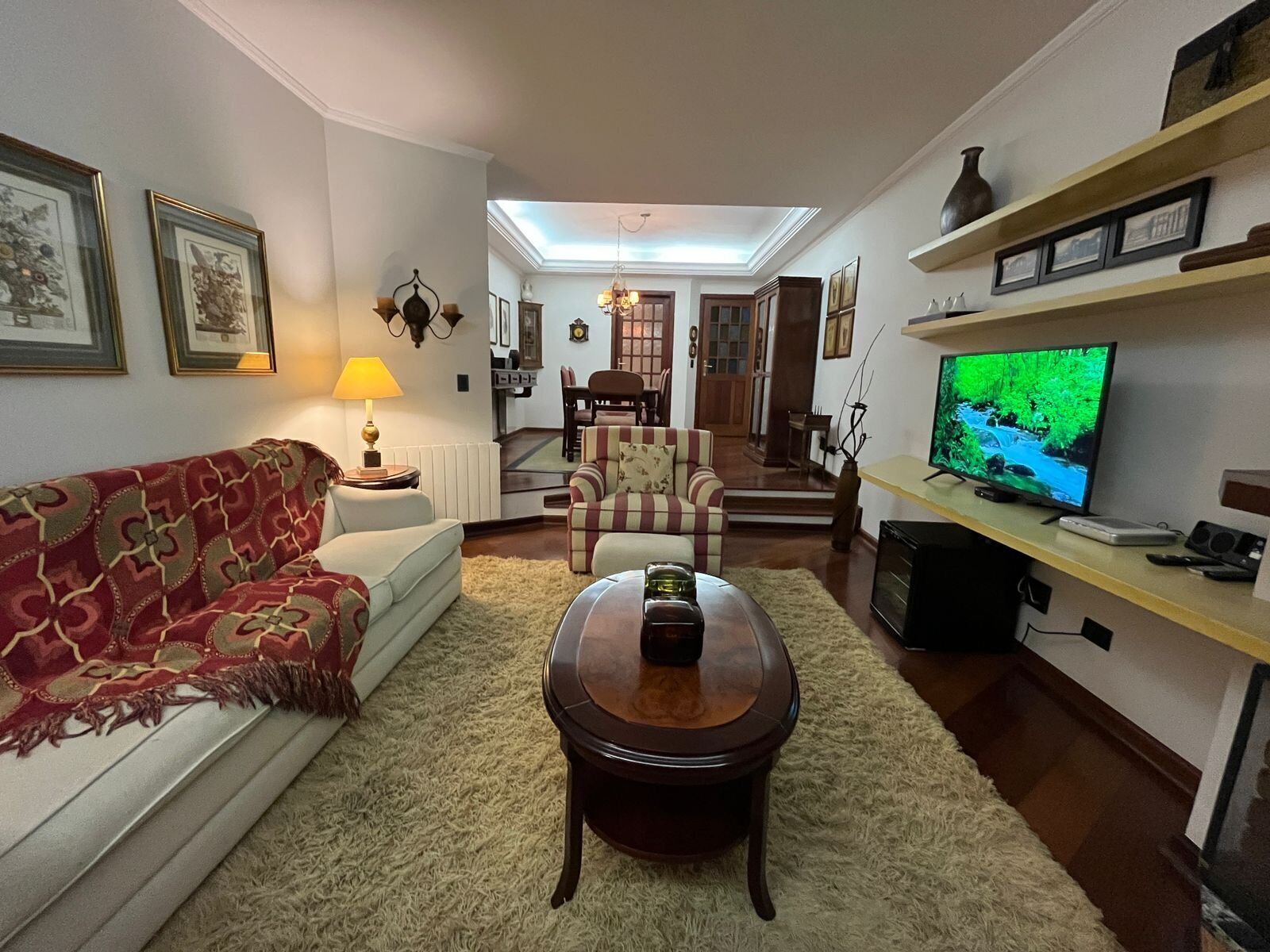 Ein Wohnzimmer mit Sofa, Sessel, Couchtisch, Fernseher und einem Essbereich im Hintergrund.