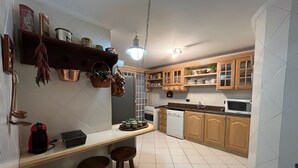 Keittiössä on puukuvioiset kaapit, valkoinen työtaso, pesuallas, mikroaaltouuni ja riippuvalaisin.