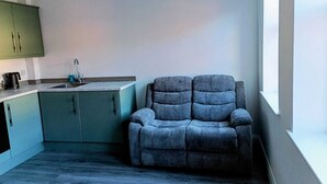 Eine moderne Küche mit Türkis-Schränken, einer schwarzen Kaffeemaschine und einem grauen Sofa in der Nähe eines Fensters.