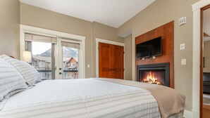 Ein Hotelzimmer mit einem großen Bett, einem Kamin, einem an der Wand befestigten Fernseher und Blick auf umliegende Gebäude.