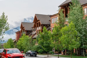 A row of modern wooden buildings with balconies, surrounded by lush green trees and a mountain backdrop. - Solara Suite-Indoor Pool - Hot tub - GYM (Canmore)