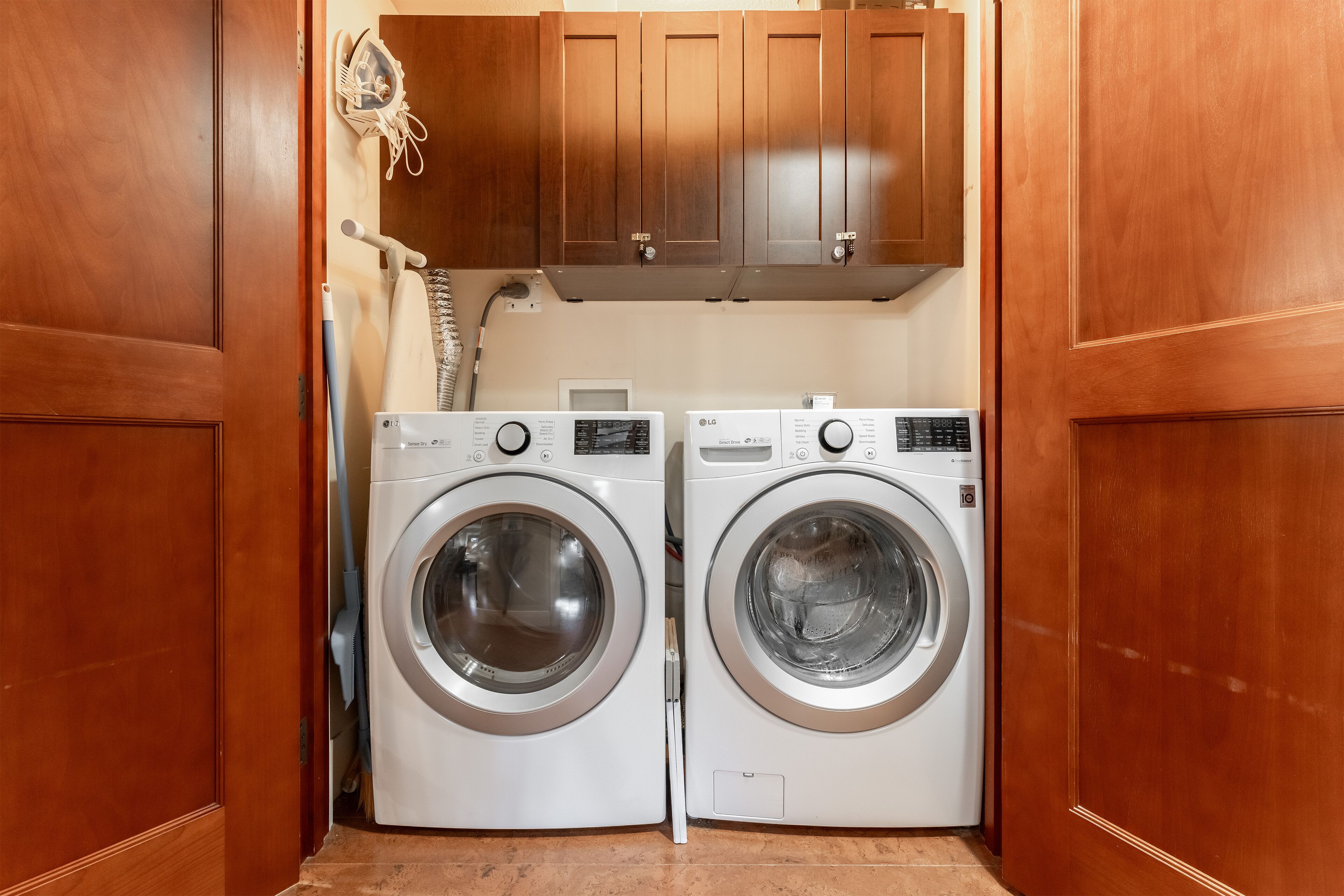 A laundry room with two front-loading washing machines and wooden cabinets above.