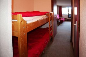 A bunk bed with red bedding in a room with a carpeted floor and a door leading to another room.