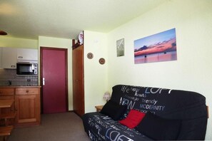 A compact living space with a kitchenette, a red door, a black sofa with motivational words, and a sunset painting on the wall.