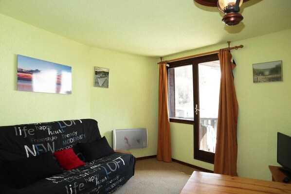 A room with a sofa, a window with curtains, a ceiling fan, and a flat-screen TV.