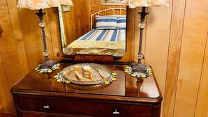 A wooden-paneled room with a bed, two bedside lamps, a mirror, and a dresser with a tray of toiletries. - Charming Door County cottage steps from Lake Michigan Beach in Jacksonport WI (Sturgeon Bay)