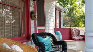 A porch with wicker furniture, a red door, and a window with a wreath. - Charming Door County cottage steps from Lake Michigan Beach in Jacksonport WI (Sturgeon Bay)