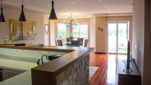 A modern kitchen with a central island, pendant lighting, and a dining area with a chandelier. - Apartamento Morro do Elefante (Campos do Jordão)
