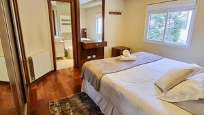 A bedroom with a bed, a nightstand, a dresser, a mirror, a window, and a radiator. - Apartamento Morro do Elefante (Campos do Jordão)