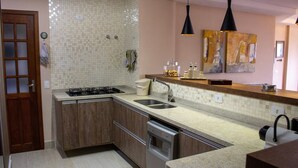 A kitchen with a stove, sink, and dishwasher, wooden cabinets, and a tiled backsplash. - Apartamento Morro do Elefante (Campos do Jordão)