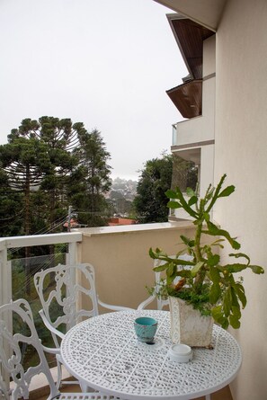 Ein Balkon mit einem weißen Tisch und Stühlen, einem Blumentopf und Blick auf Bäume und Gebäude.