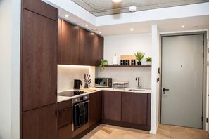 A modern kitchen with dark wood cabinets, a built-in oven, and a countertop with a coffee maker and toaster. - The Mancunian Skyline | Chic 1BR City View w/ Wifi (Manchester)
