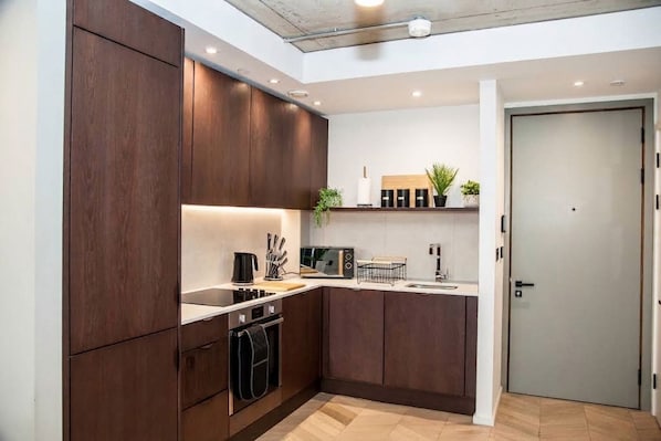 Una cocina moderna con armarios de madera oscura, horno empotrado y encimera con cafetera y tostadora.