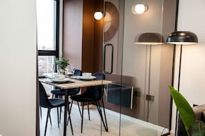 Un comedor moderno con un separador de vidrio, una mesa de madera, sillas negras y una lámpara de pie.