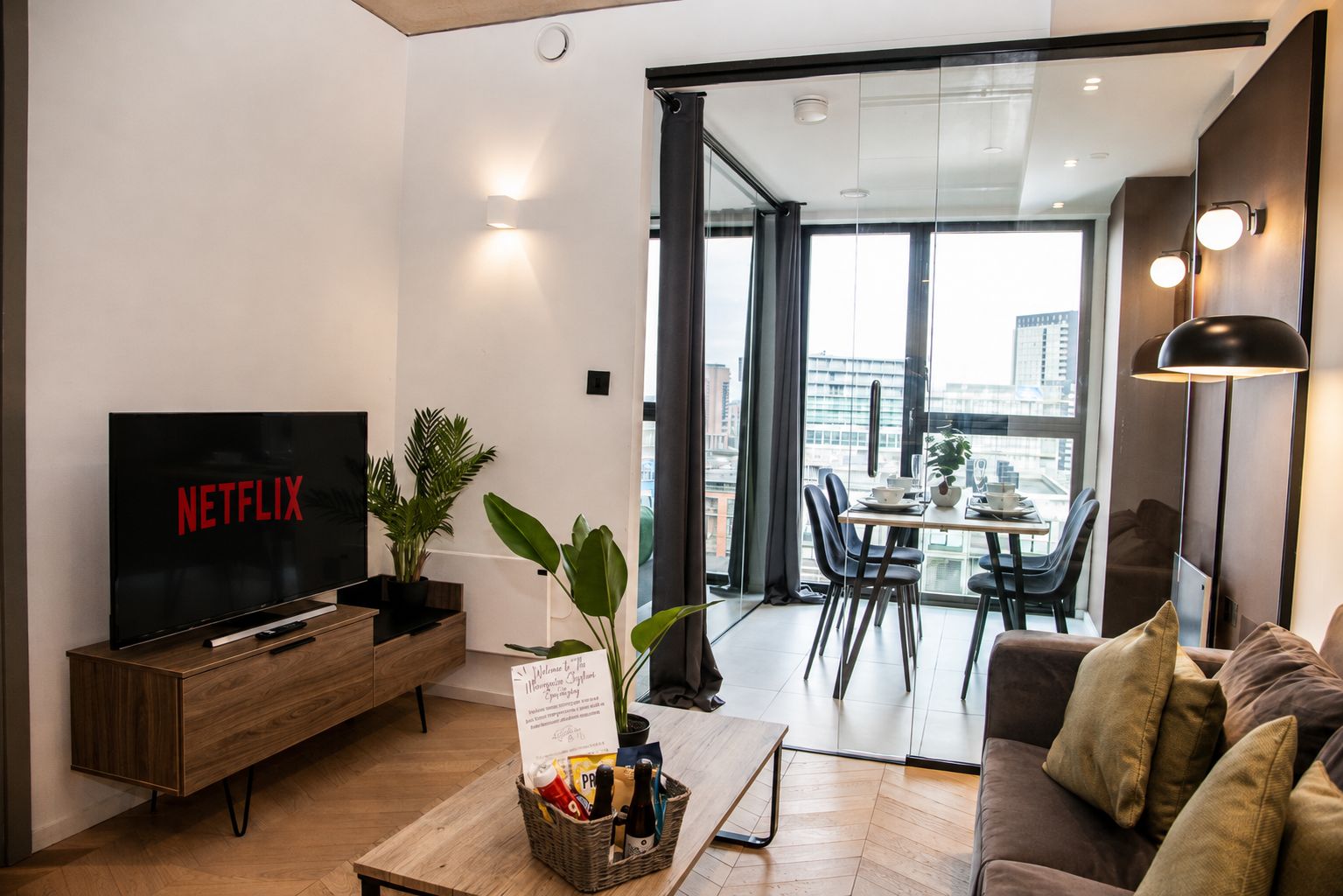 A modern living room with a flat-screen TV, a wooden coffee table, a sofa, and a dining area with a table and chairs.