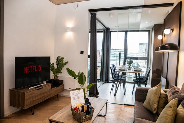 A modern living room with a flat-screen TV, a wooden coffee table, a sofa, and a dining area with a table and chairs.