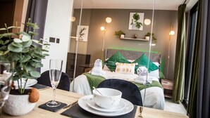 Hotellihuone, jossa on sänky, yöpöytä ja ruokailutila, jossa on pöytä kahdelle henkilölle katettuna.