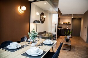 A dining area with a wooden table set for four, a potted plant, and a wall-mounted clock. - The Mancunian Skyline | Chic 1BR City View w/ Wifi (Manchester)