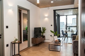 Una sala de estar moderna con televisor de pantalla plana, muebles de madera, un comedor con mesa y sillas, y un amplio ventanal con vista a la ciudad.