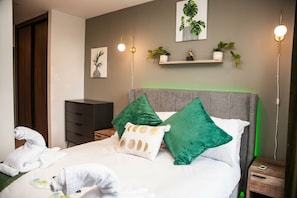 Habitación de hotel con una cama, mesita de noche, cómoda y repisa con plantas.