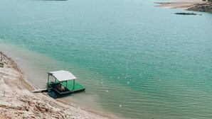 Ein Boot mit grüner Markise liegt an einem sandigen Strand an einem ruhigen, türkisblauen See.