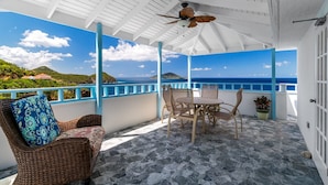 A covered outdoor seating area with a table and chairs, a wicker chair with a cushion, and a potted plant. - Seahorse Oceanfront Villa with Pool & Hot Tub! USVI (St Thomas)