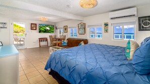 A bedroom with a large bed, a view of the beach, and a dining area with chairs. - Seahorse Oceanfront Villa with Pool & Hot Tub! USVI (St Thomas)
