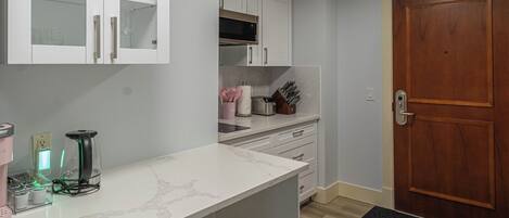 A modern kitchen with white cabinets, a marble countertop, and a wooden door.