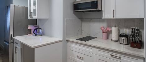 Een moderne keuken met witte kasten, een magnetron, een broodrooster en een koffiezetapparaat.
