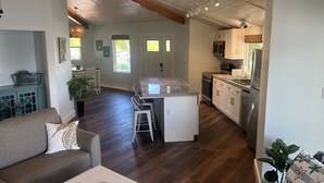 A spacious living area with a kitchen and dining area, wooden flooring, and a high ceiling with exposed beams.