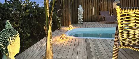 A wooden deck with a pool, a Buddha statue, and a chair.