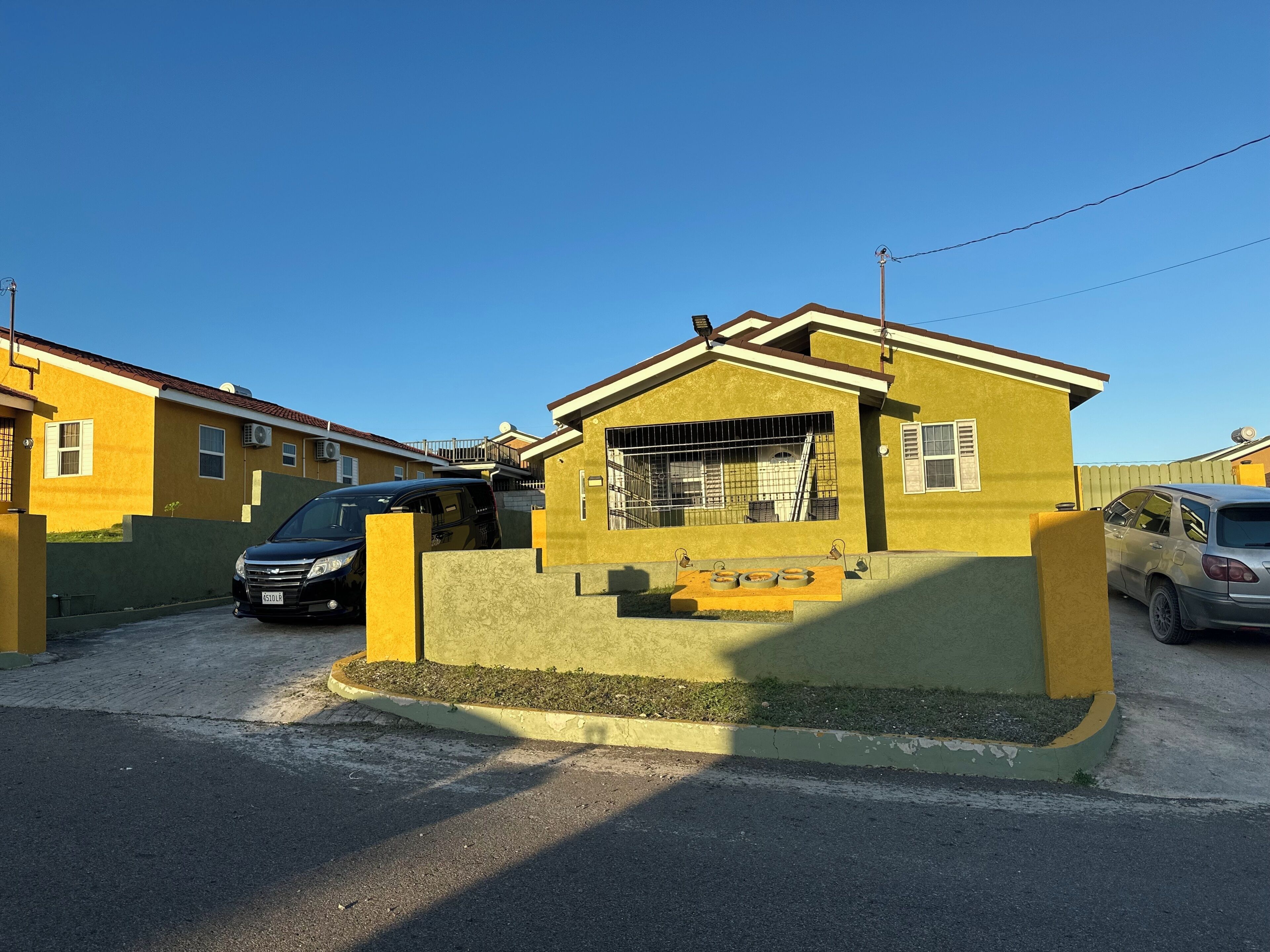 A residential area with houses, a gated entrance, and parked cars.