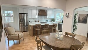 A modern kitchen with white cabinets, stainless steel appliances, and a wooden dining table with chairs. - Spacious & Charming Home  (Portland)