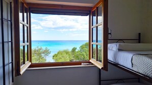 Ein Zimmer mit großem Fenster mit Blick auf Strand und Meer, einem Etagenbett und einem kleinen Nachttisch.