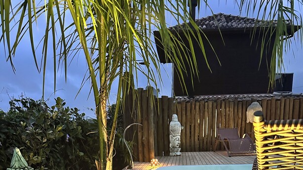 Una terrassa de fusta amb una piscina, una estàtua de Buda i una cadira.