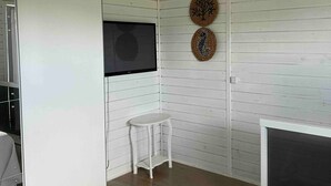 Una habitació amb un llit, una taula petita blanca, un televisor penjat i decoració mural.