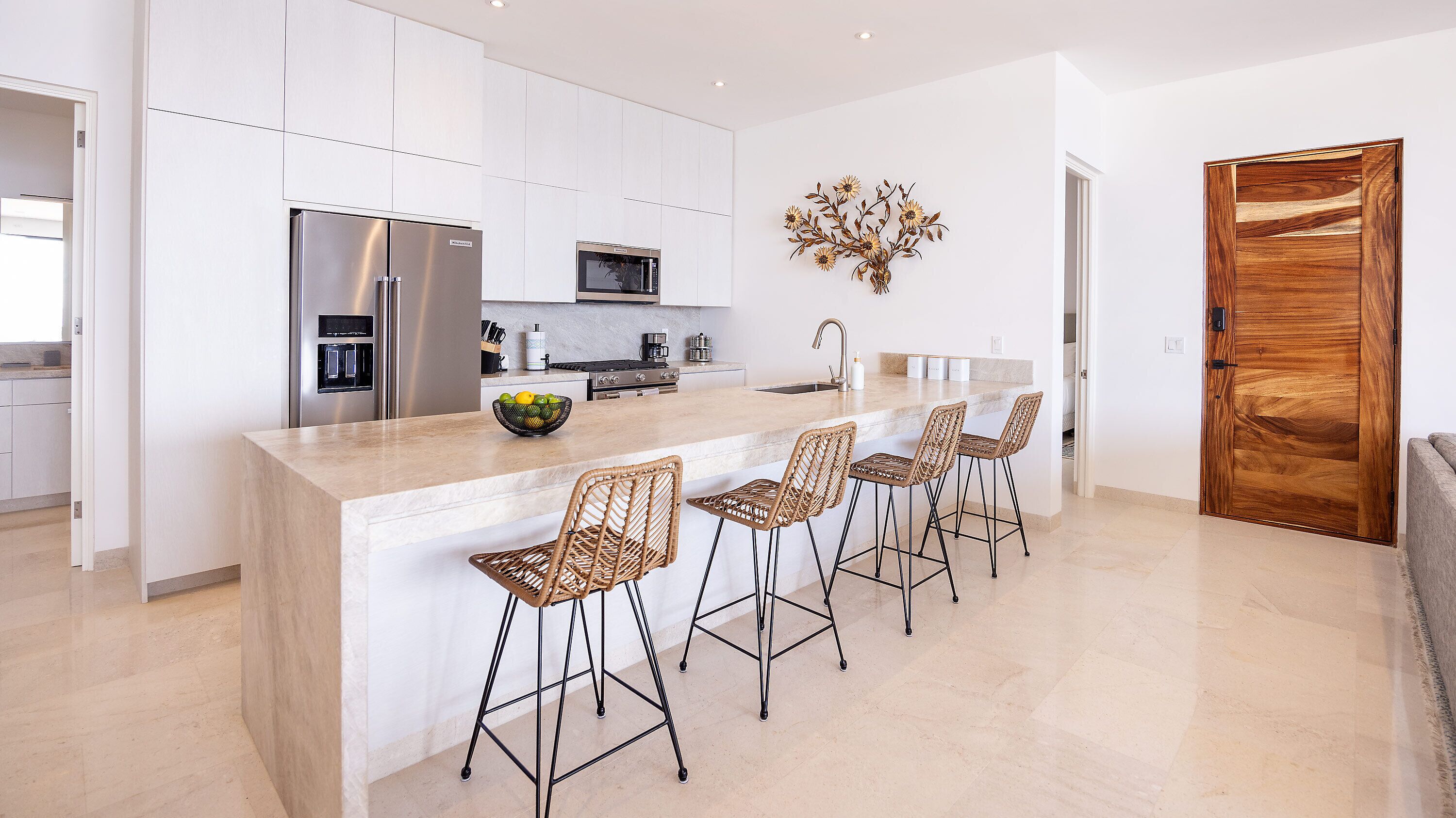 A modern kitchen with white cabinetry, a stainless steel refrigerator, a microwave, and a large island with bar stools.