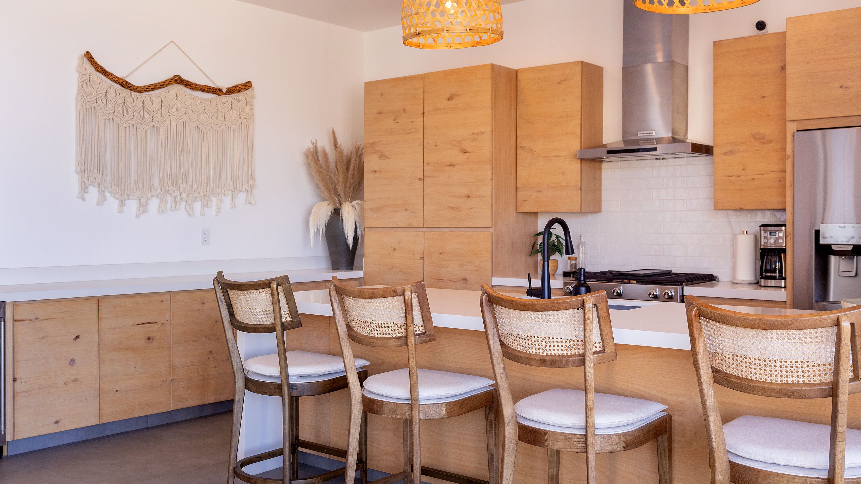 Una cocina moderna con armarios de madera, una isla central con taburetes y un adorno colgante de macramé.