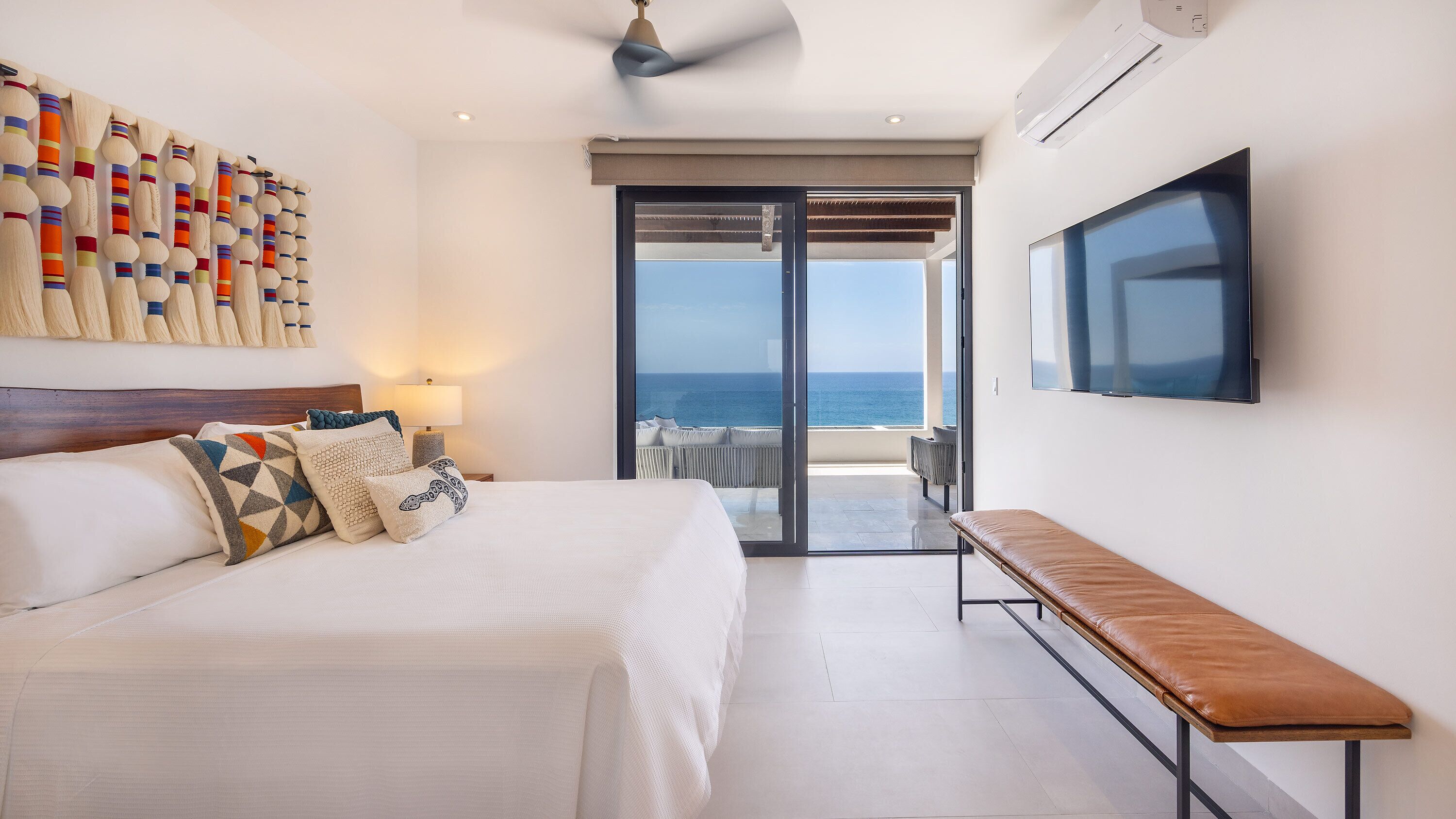 Un dormitorio con cama, un banco, un televisor y vista al mar.