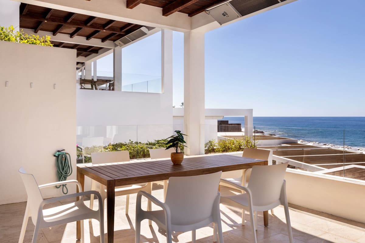 A balcony with a wooden table and chairs, overlooking the sea.