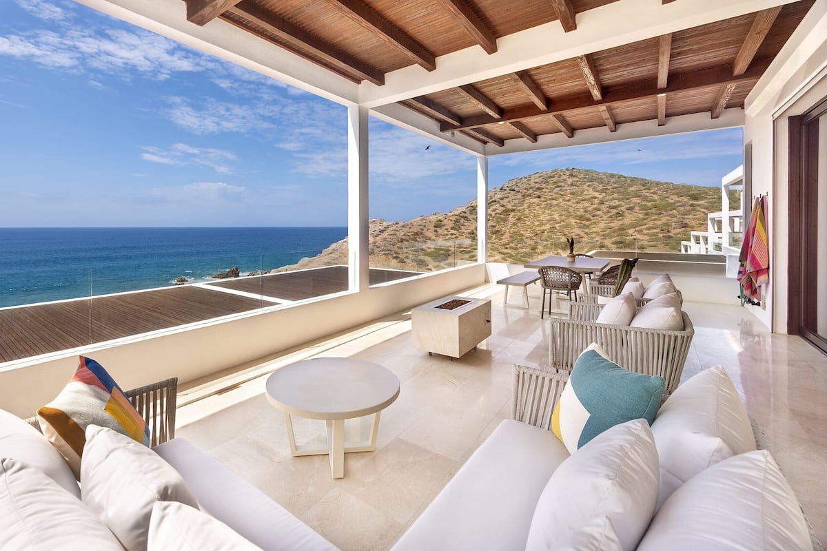 A balcony with a view of the sea, white outdoor furniture, and a wooden ceiling.