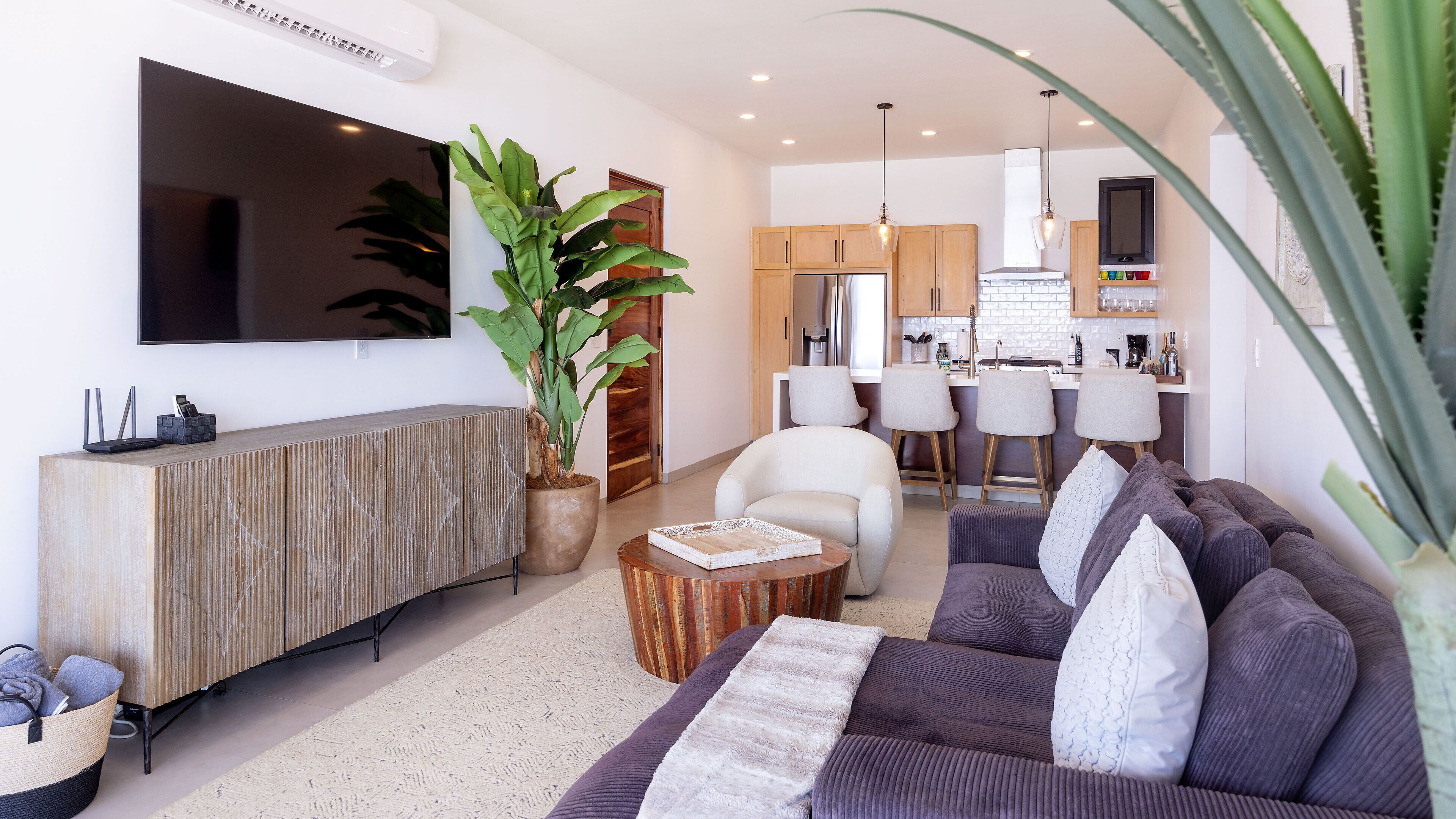 A modern living room with a large TV, a sofa, a coffee table, and a potted plant.