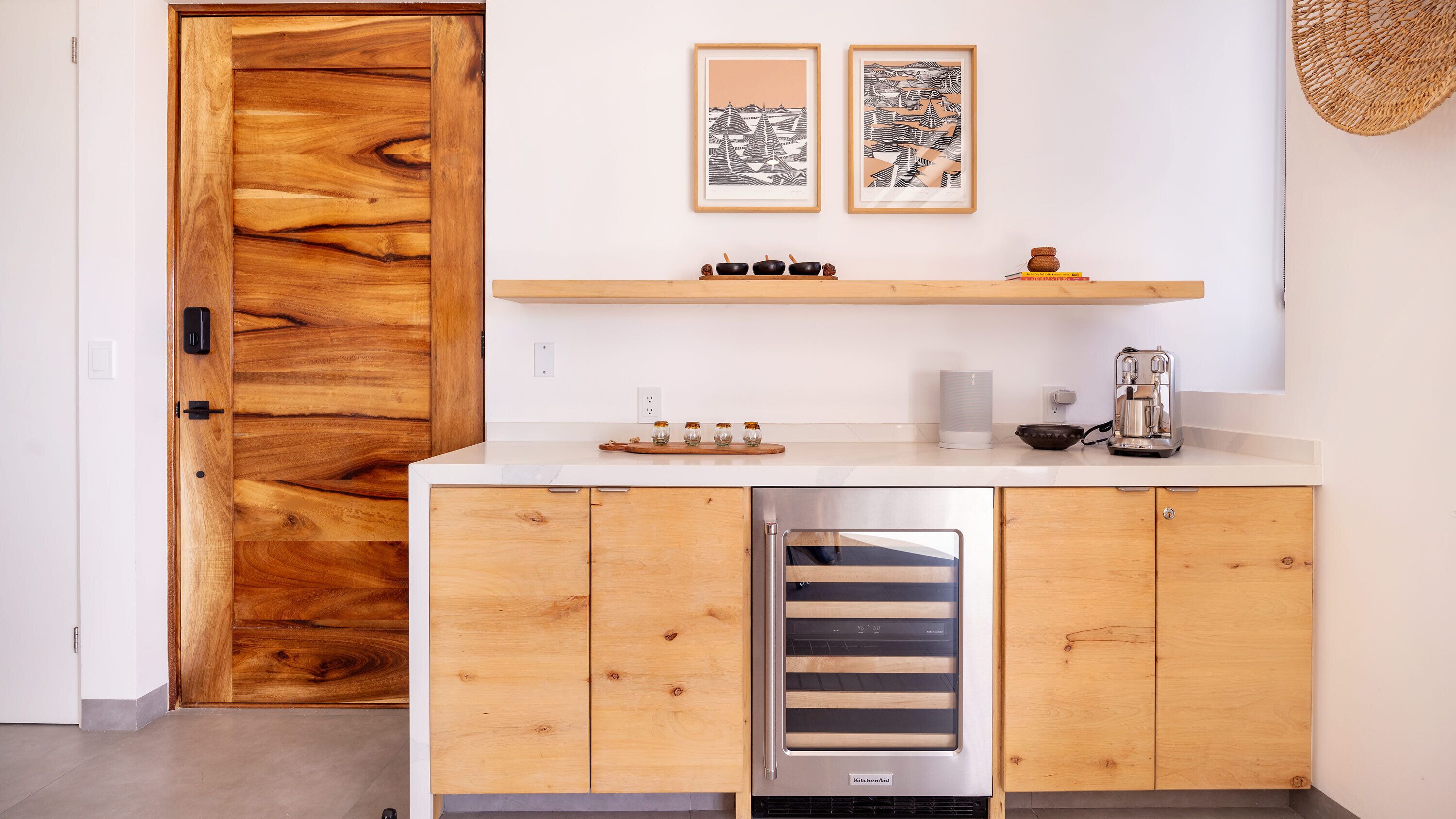 Une cuisine compacte avec des meubles en bois, un four encastré et une machine à café. Deux œuvres d’art encadrées sont accrochées au-dessus du plan de travail.