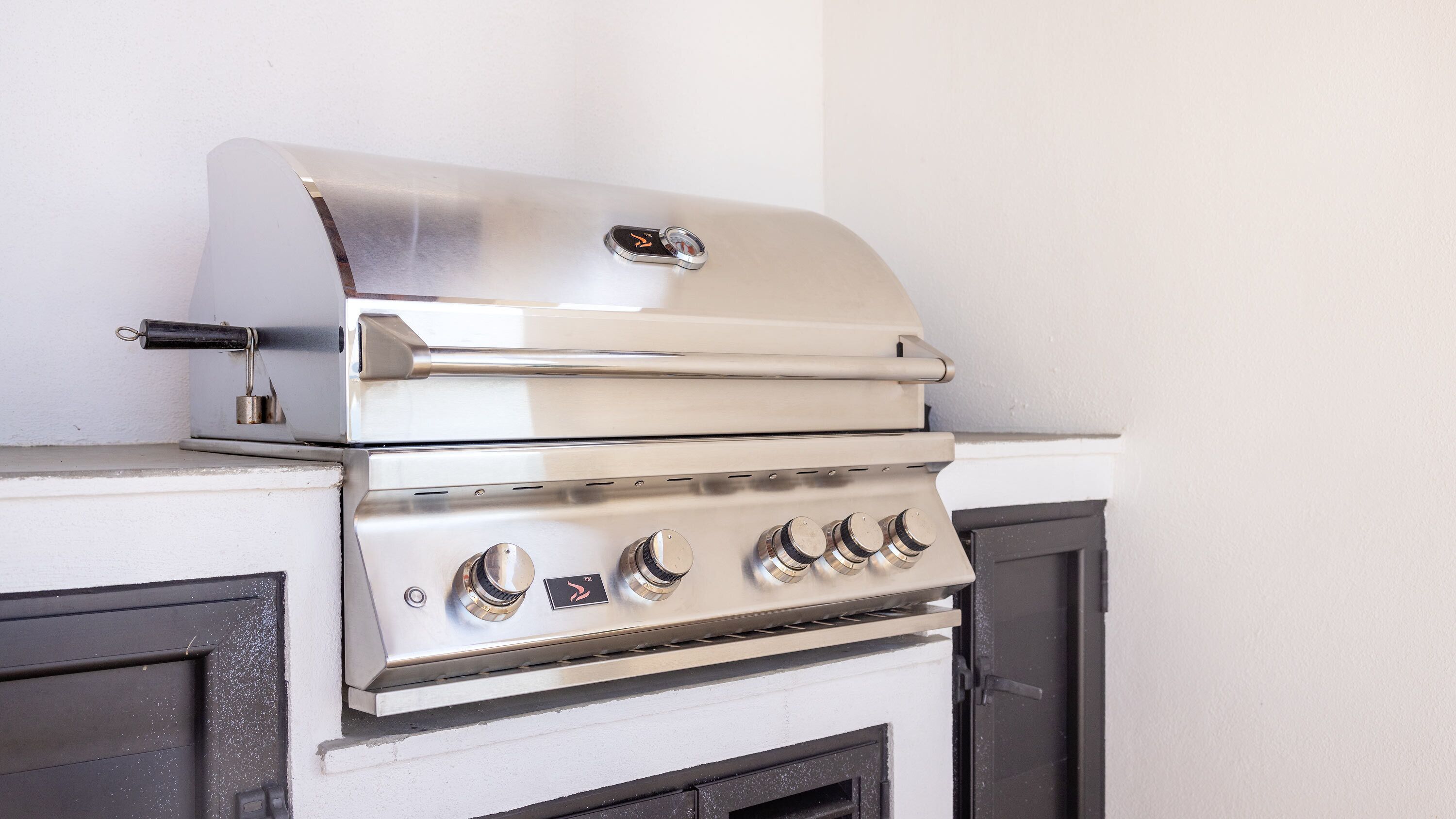 A stainless steel gas grill with a lid and four burners, mounted on a white cabinet with a black door.