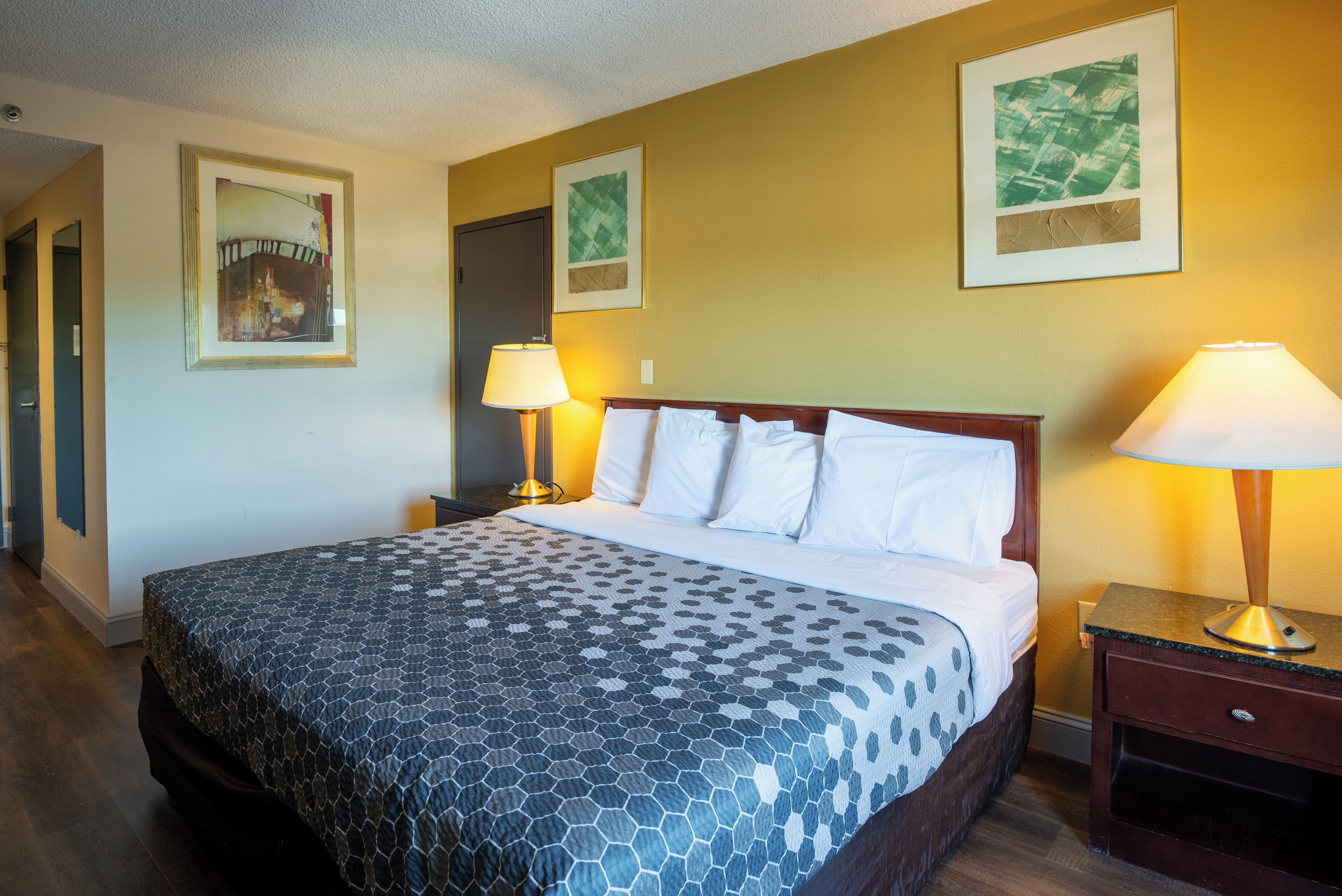 A hotel room with a large bed, two bedside lamps, and two framed pictures on the wall.